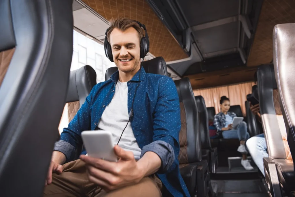 happy-adult-man-in-headphones-listening-music-and-using-smartphone-during-trip-on-bus